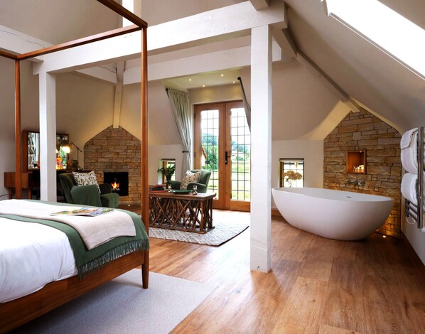 Un dormitorio con cama con dosel, chimenea de piedra, un gran ventanal y un baño independiente con bañera exenta.