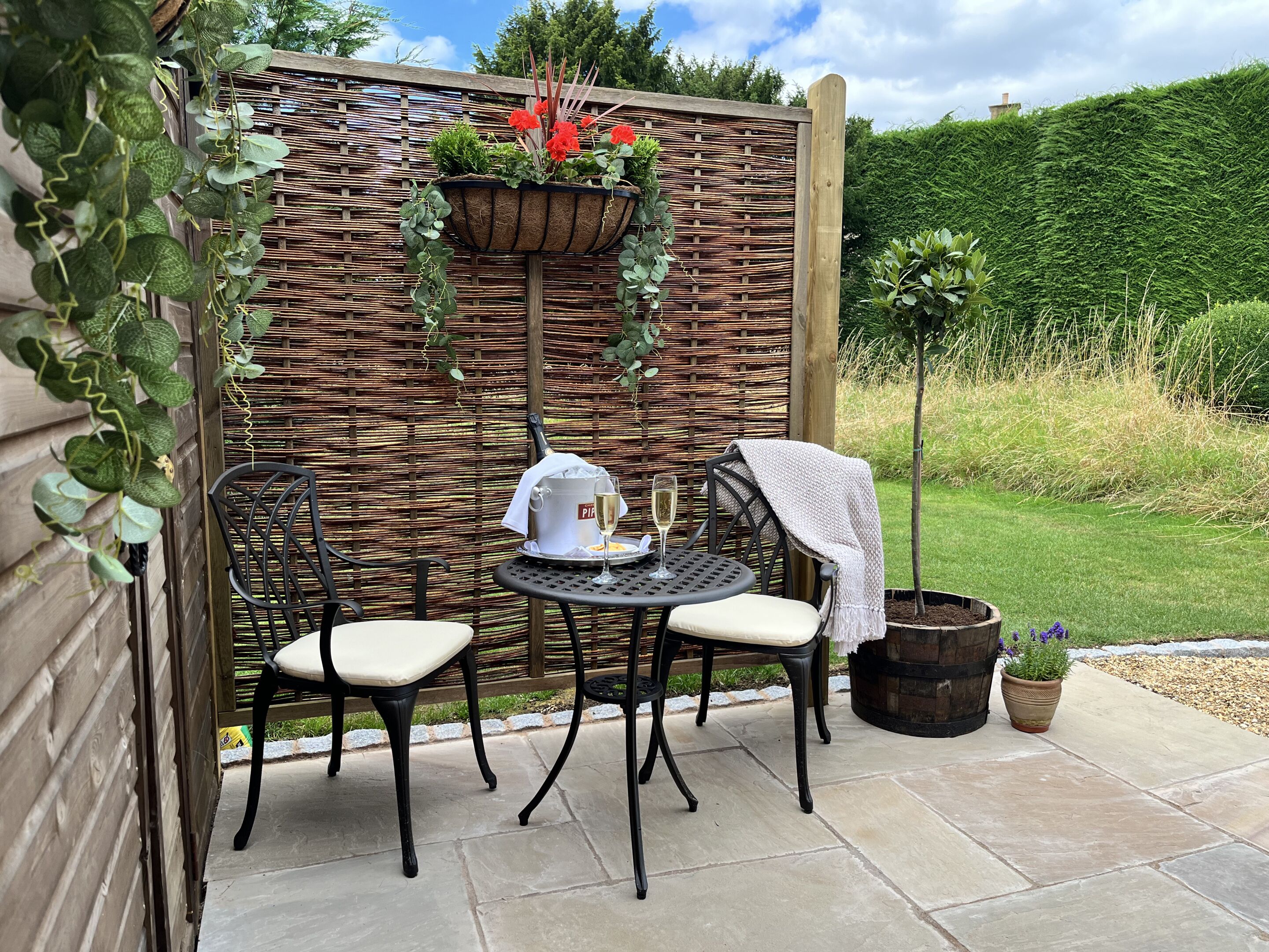 A patio with two chairs, a table, a wine glass, and a potted plant.