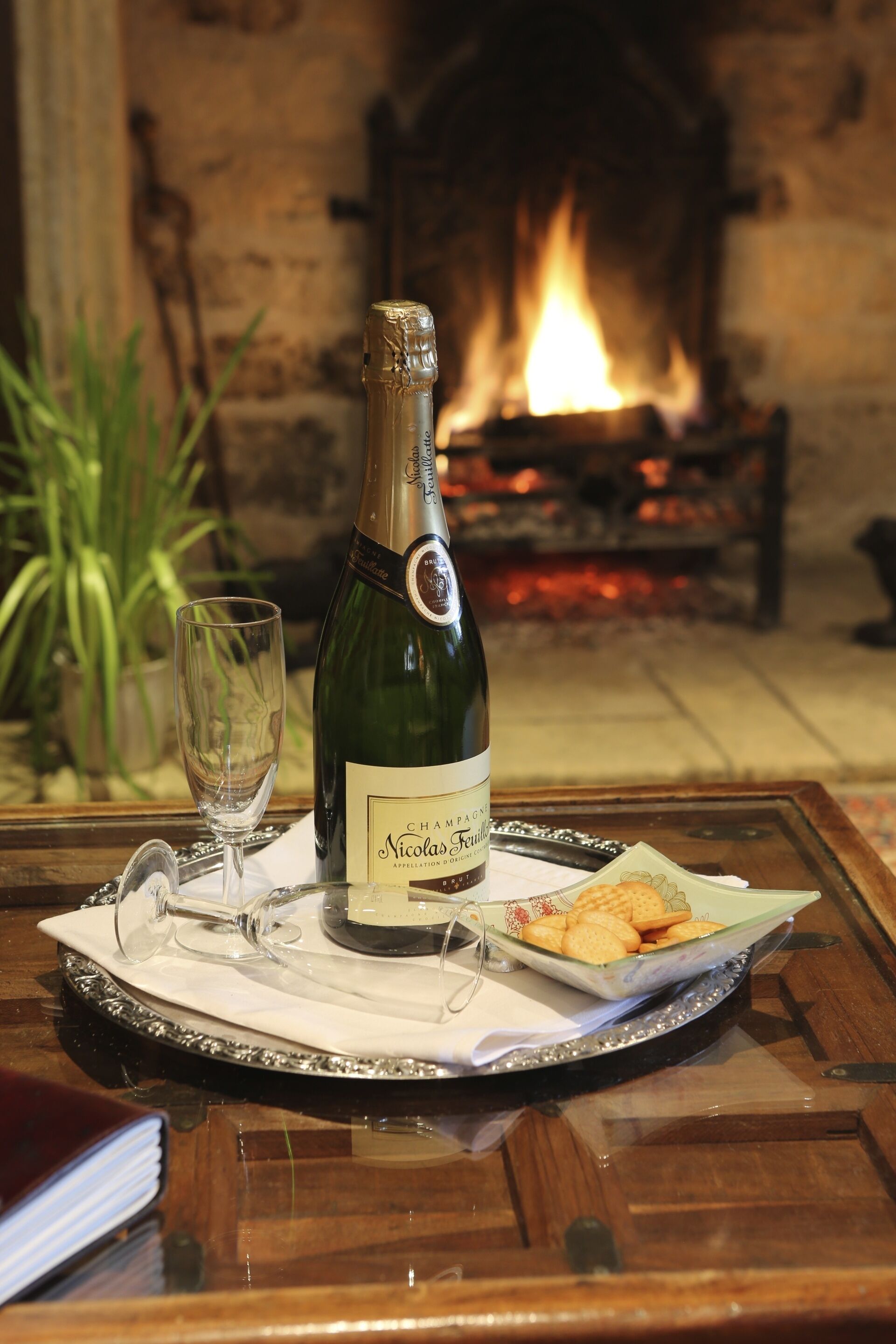 A bottle of Nicolas Feuillier champagne, a glass, and crackers on a tray.