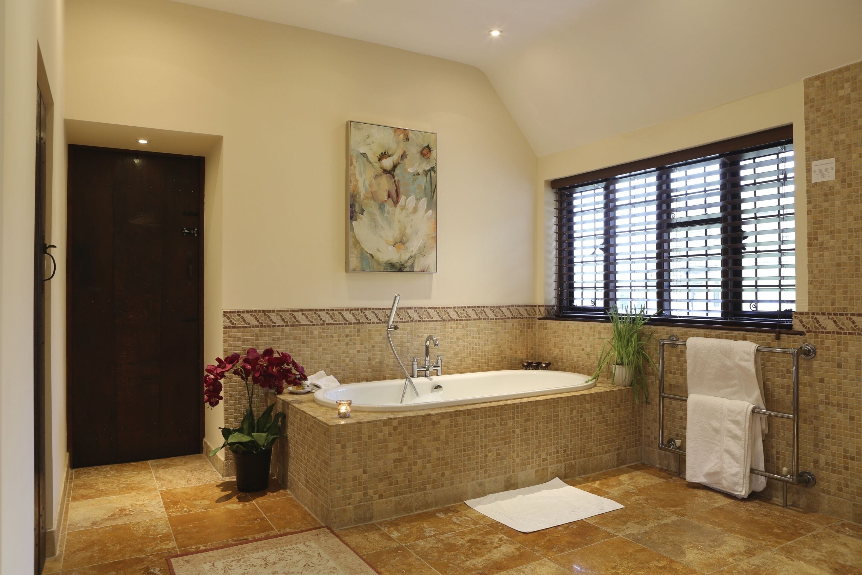 Ein Badezimmer mit einer großen Badewanne, einem Fenster mit Jalousien, einem Handtuchhalter und einem Blumentopf.