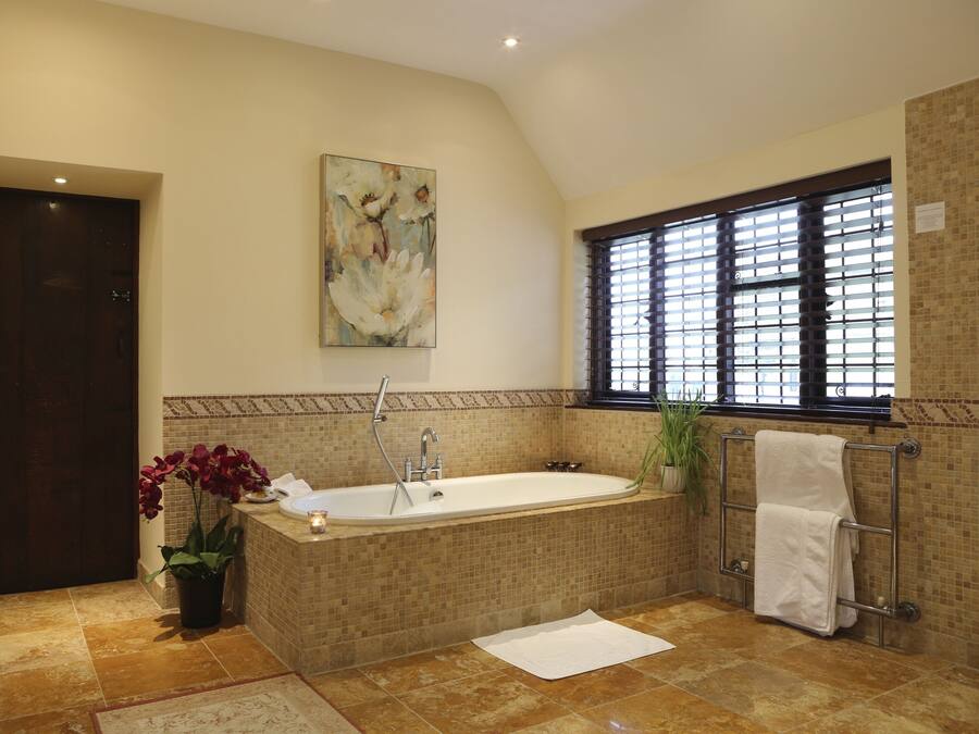 Ein Badezimmer mit einer großen Badewanne, einem Fenster mit Jalousien, einem Handtuchhalter und einem Blumentopf.