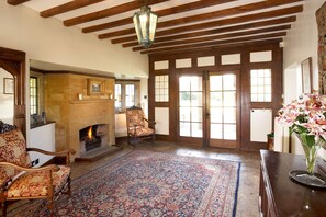 A traditional room with a fireplace, patterned rug, wooden furniture, and a large window with multiple panes. - Abbots Grange Manor House (Broadway)