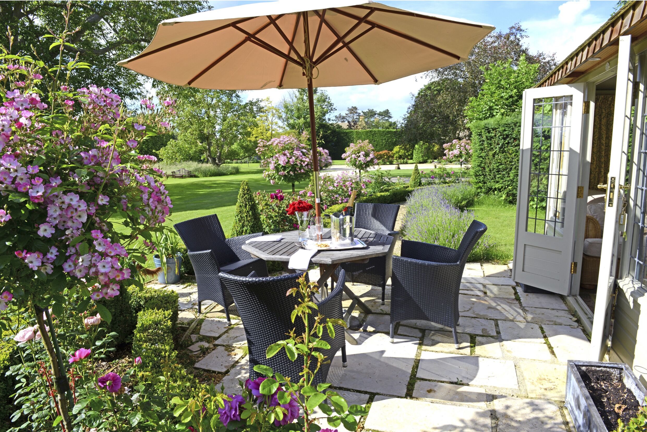 An outdoor patio with a table and chairs, surrounded by lush greenery and flowers.