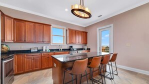 A kitchen with wooden cabinets, a large island with bar stools, and a pendant light. - Big Balcony Breezes/Valhalla Laguna Key (Gulf Shores)