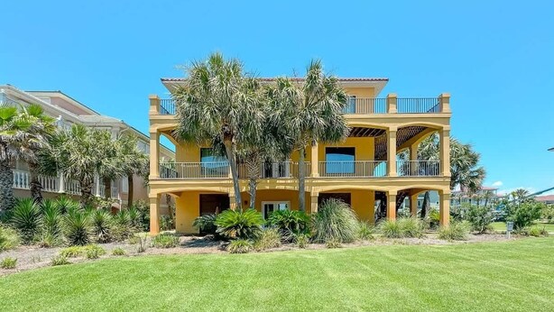 A two-story yellow building with balconies, surrounded by a well-maintained lawn and palm trees. - Big Balcony Breezes/Valhalla Laguna Key (Gulf Shores)