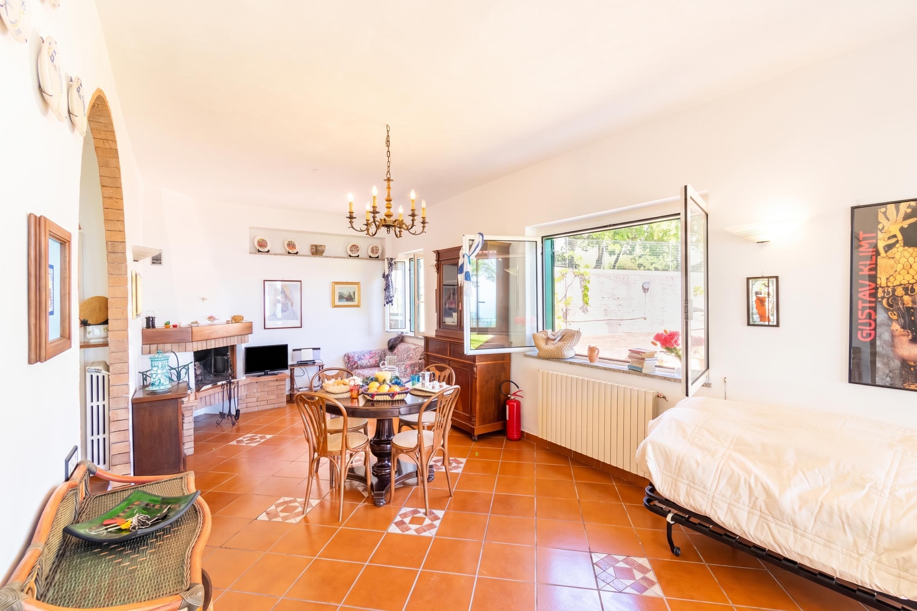 Une pièce confortable avec un lit, une table à manger, des chaises, un lustre et une vue par la fenêtre.
