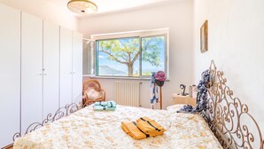 Ein Schlafzimmer mit Bett, Kleiderschrank, Fenster mit Blick auf einen Baum und einem Sessel.