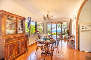 A dining area with a table set for four, surrounded by wooden chairs, a chandelier, and a view of the outdoors.