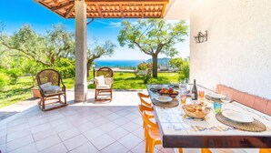Eine Terrass mit Esstisch, Korbstühlen und Blick auf das Meer.