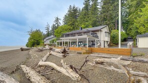 A coastal property with a large deck and multiple rooms, surrounded by natural scenery and a beach.