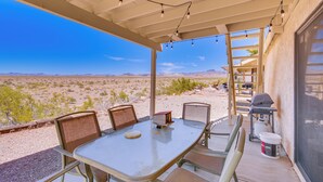 A covered patio with a table and chairs, a grill, and a view of the desert landscape.