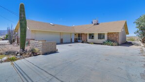 A single-story house with a garage, a large cactus in the front yard, and a clear blue sky.