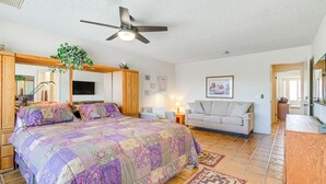 A bedroom with a large bed, a ceiling fan, a TV, a sofa, and a wooden cabinet.