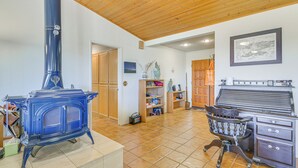 A room with a blue wood-burning stove, wooden cabinets, a chair, and a piano.