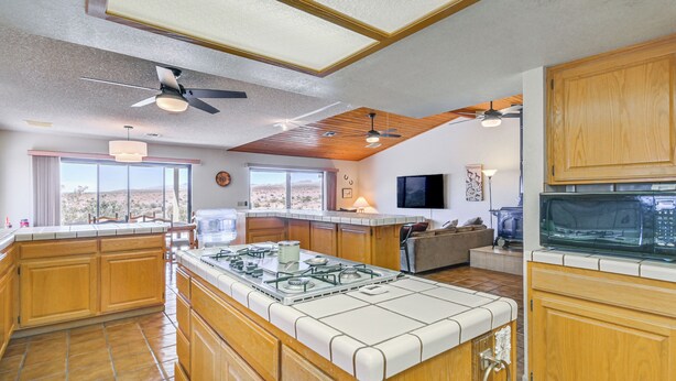 A spacious kitchen with wooden cabinets, a central island with a gas stove, and large windows offering a view of the desert.