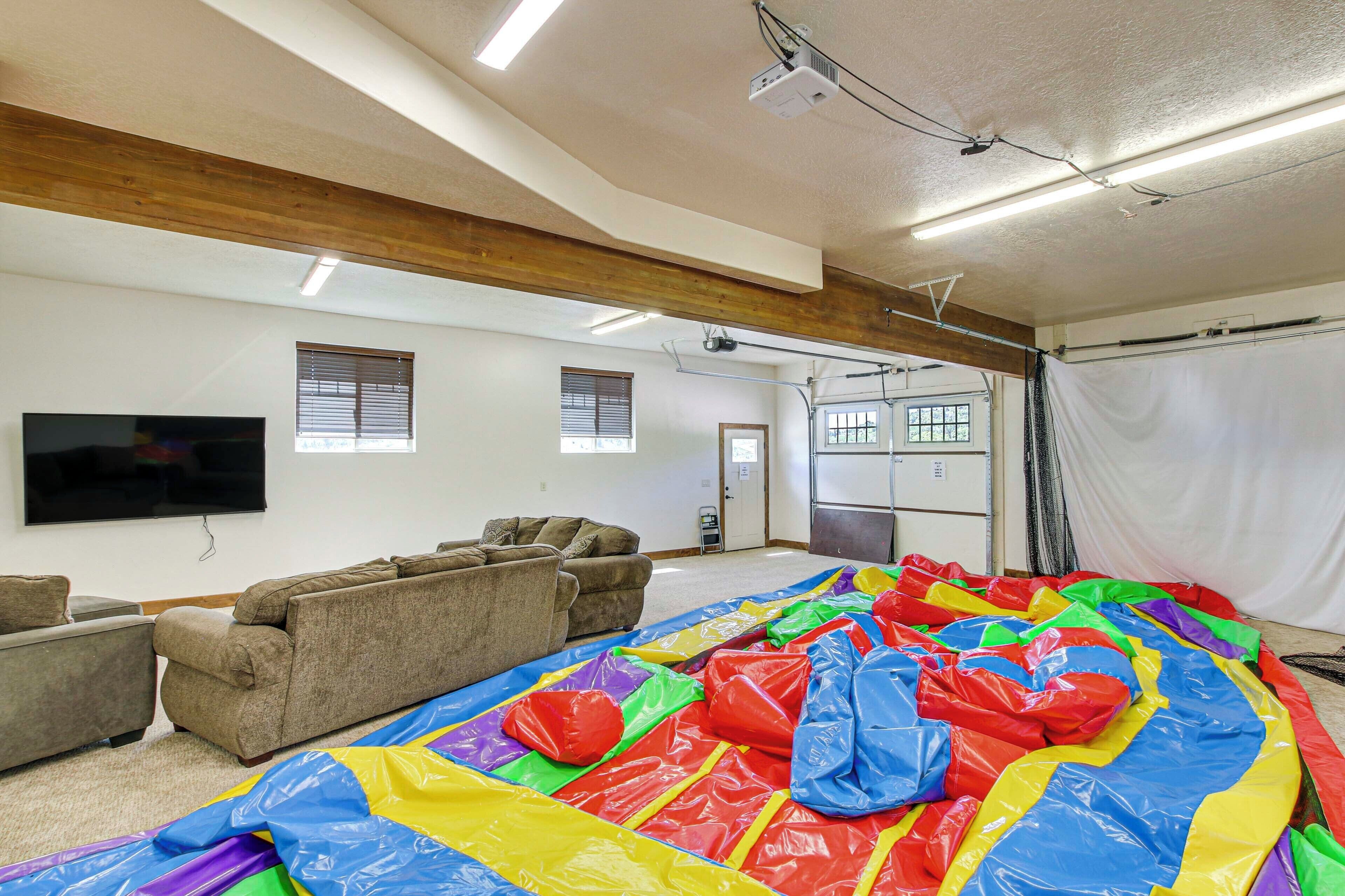 A spacious room with a large inflatable play area, multiple sofas, a flat-screen TV, and a ceiling-mounted projector.