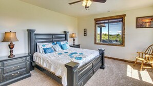 Quarto com cama, mesas de cabeceira, ventoinha no teto, janela com vista e uma cadeira.