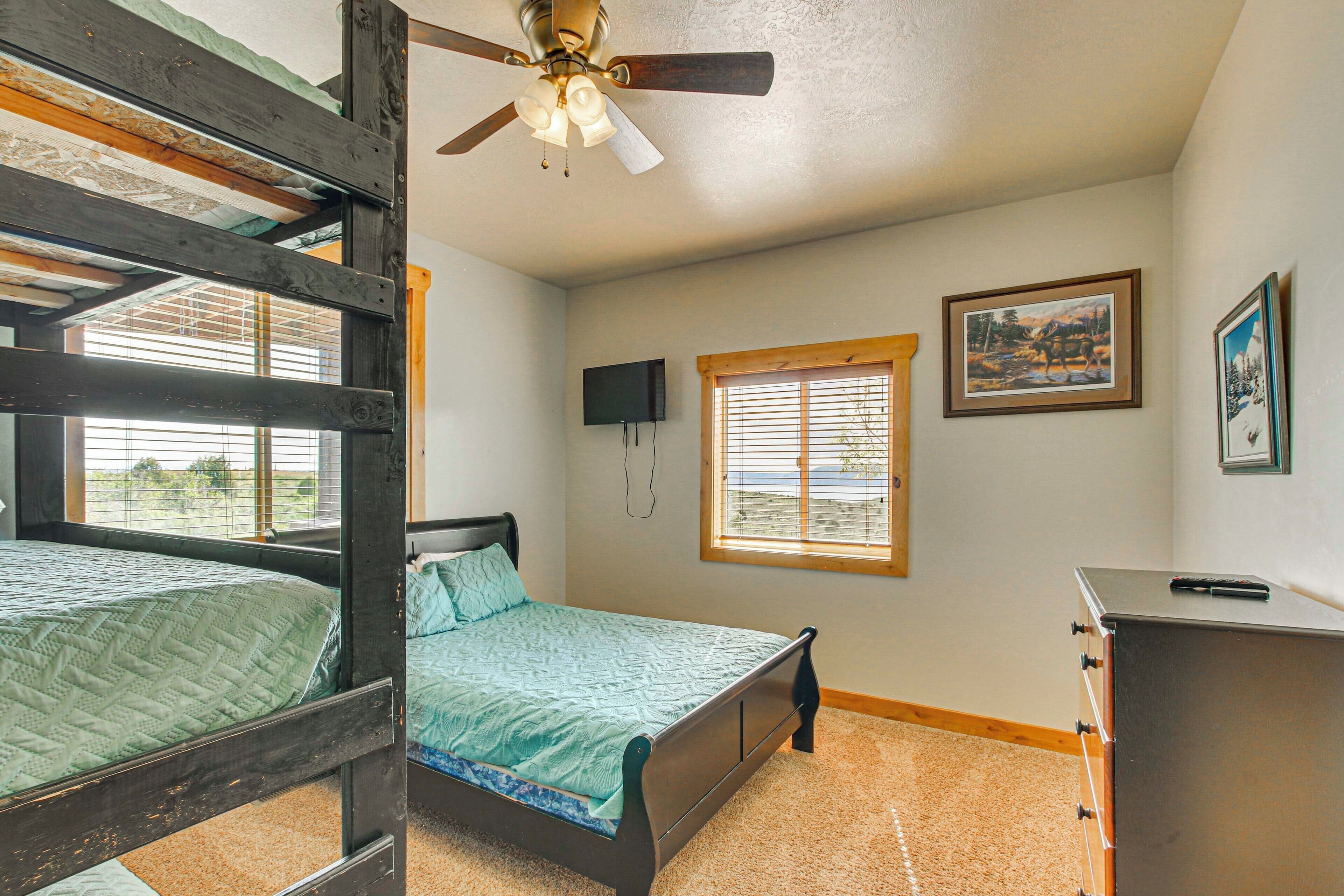 A bedroom with bunk beds, a ceiling fan, a window with blinds, and a dresser.
