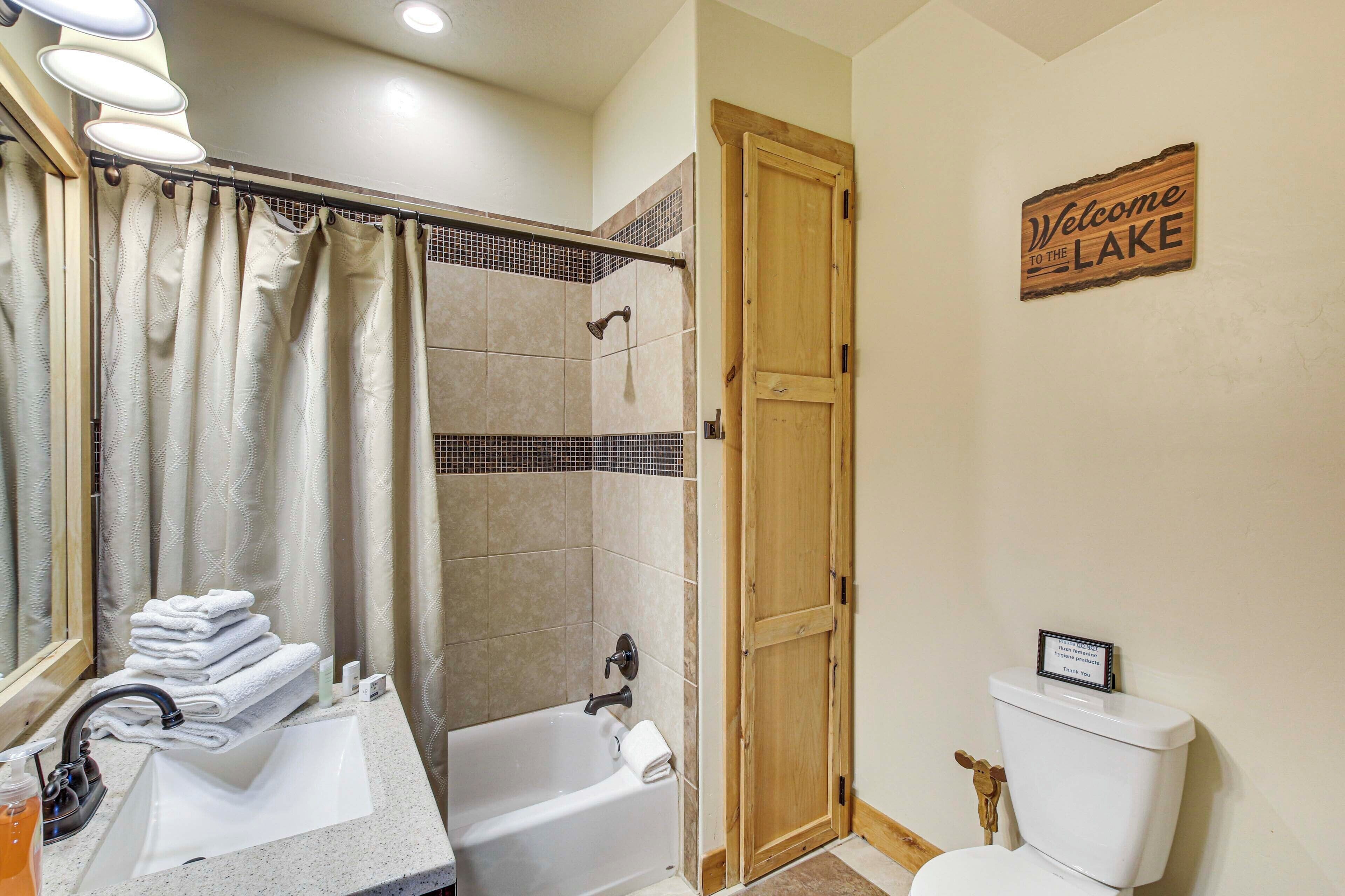 A bathroom with a bathtub, a sink, and a toilet. There is a shower curtain, a towel rack, and a welcome sign.