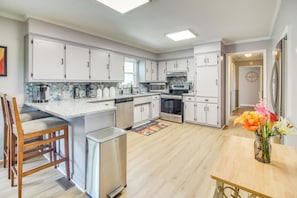 A modern kitchen with white cabinets, a stainless steel dishwasher, and a wooden dining table with a vase of flowers.