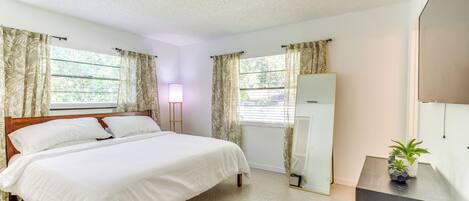 A bedroom with a bed, curtains, a bedside lamp, a mirror, and a small plant on a dresser.