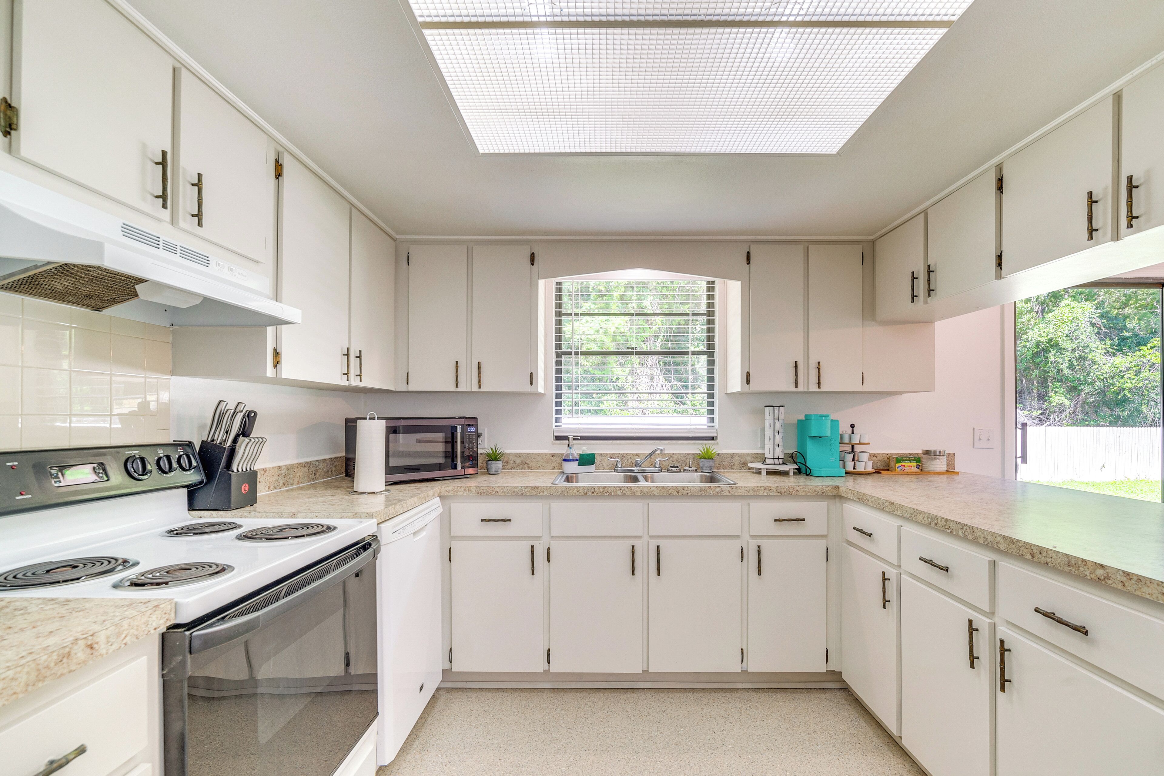 A modern kitchen with white cabinets, a gas stove, a microwave, and a window providing natural light.