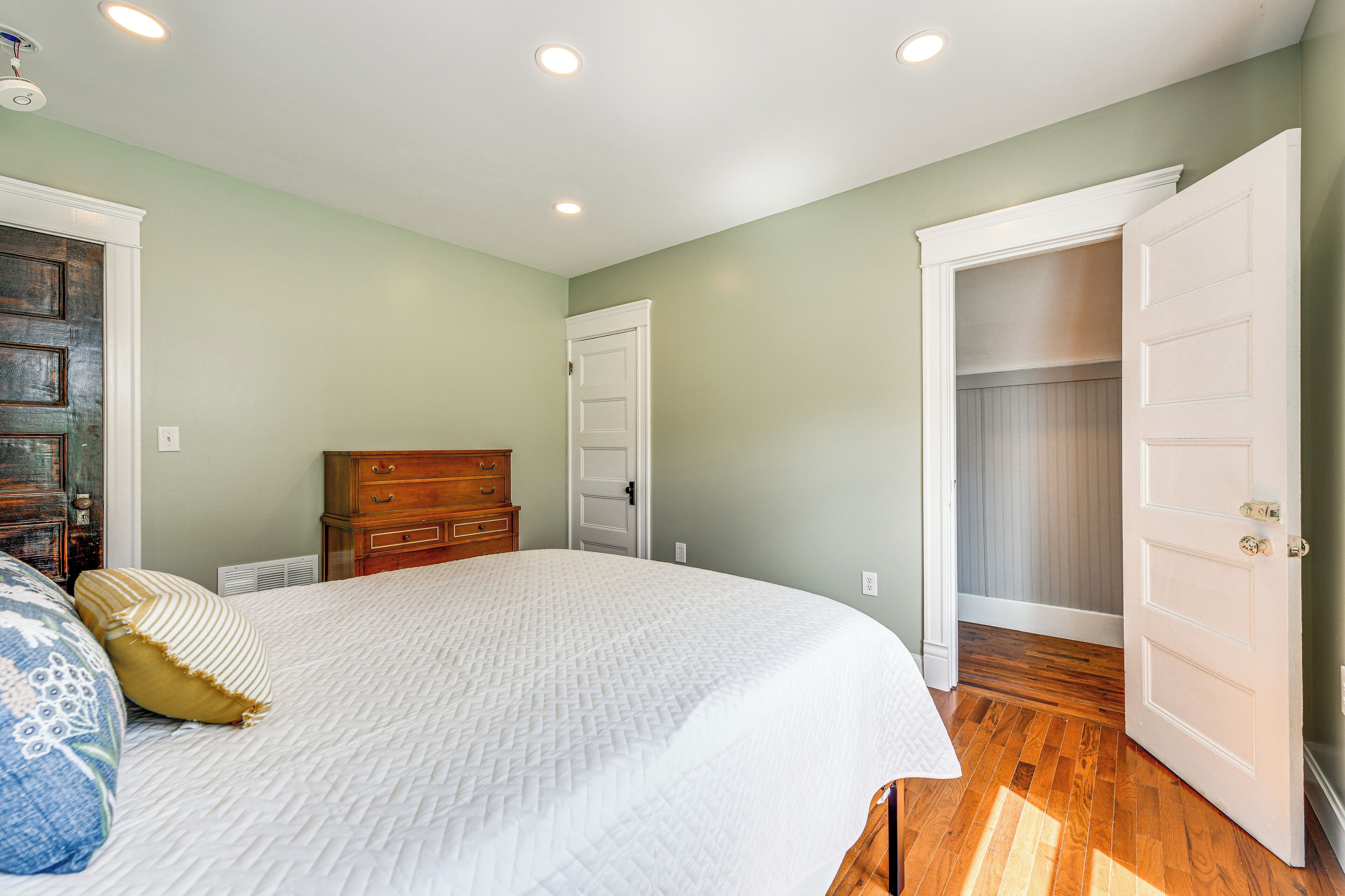 A bedroom with a large bed, wooden dresser, and a walk-in closet.