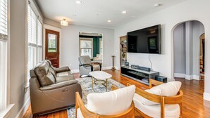 Ein modernes Wohnzimmer mit einer Ledersofa, Holzstühlen, einem Couchtisch und einem an der Wand montierten Flachbildfernseher.