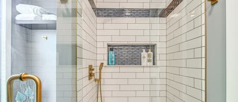 Un baño moderno con azulejos blancos tipo metro, cabina de ducha de vidrio y un pequeño estante con artículos de aseo.