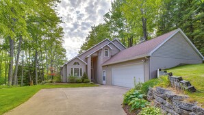 Une maison à deux étages avec un garage, entourée d’une pelouse bien entretenue et d’arbres.