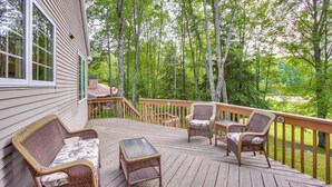 Une terrasse en bois, agrémentée de meubles en osier, dont un canapé et des fauteuils, donnant sur une zone boisée.
