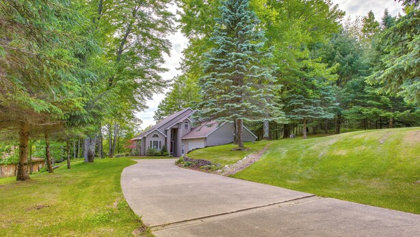 Une maison d’habitation avec une allée incurvée, entourée d’une végétation luxuriante et de grands arbres.