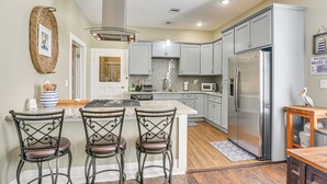 A kitchen with a central island, bar stools, a refrigerator, and a microwave.