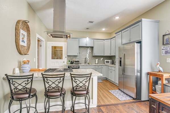 A kitchen with a central island, bar stools, a refrigerator, and a microwave.