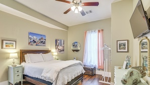 A bedroom with a bed, bedside tables, a ceiling fan, artwork, and a dresser with decorative items.