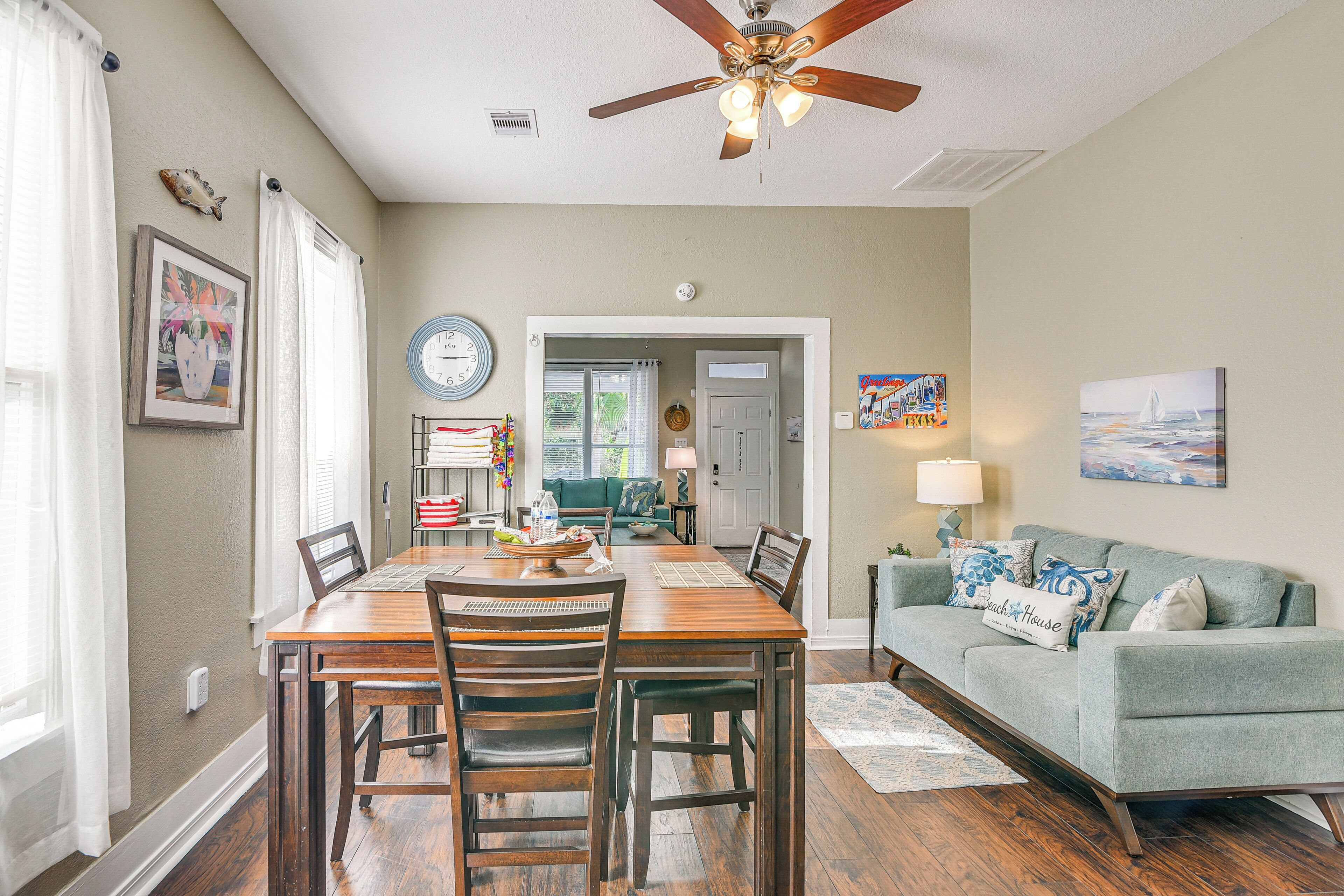 A dining area with a wooden table and chairs, a ceiling fan, and a couch in a living room.