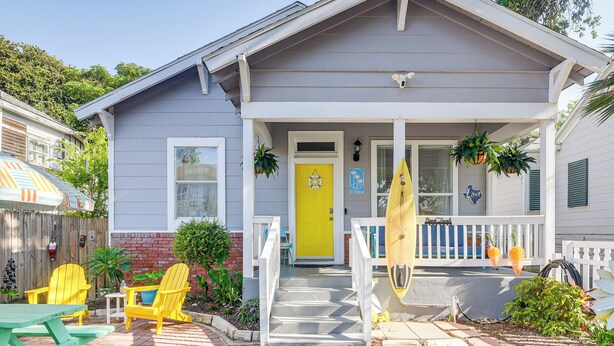 A house with a bright yellow front door, a porch with white railings, and a brick pathway leading to the front door.