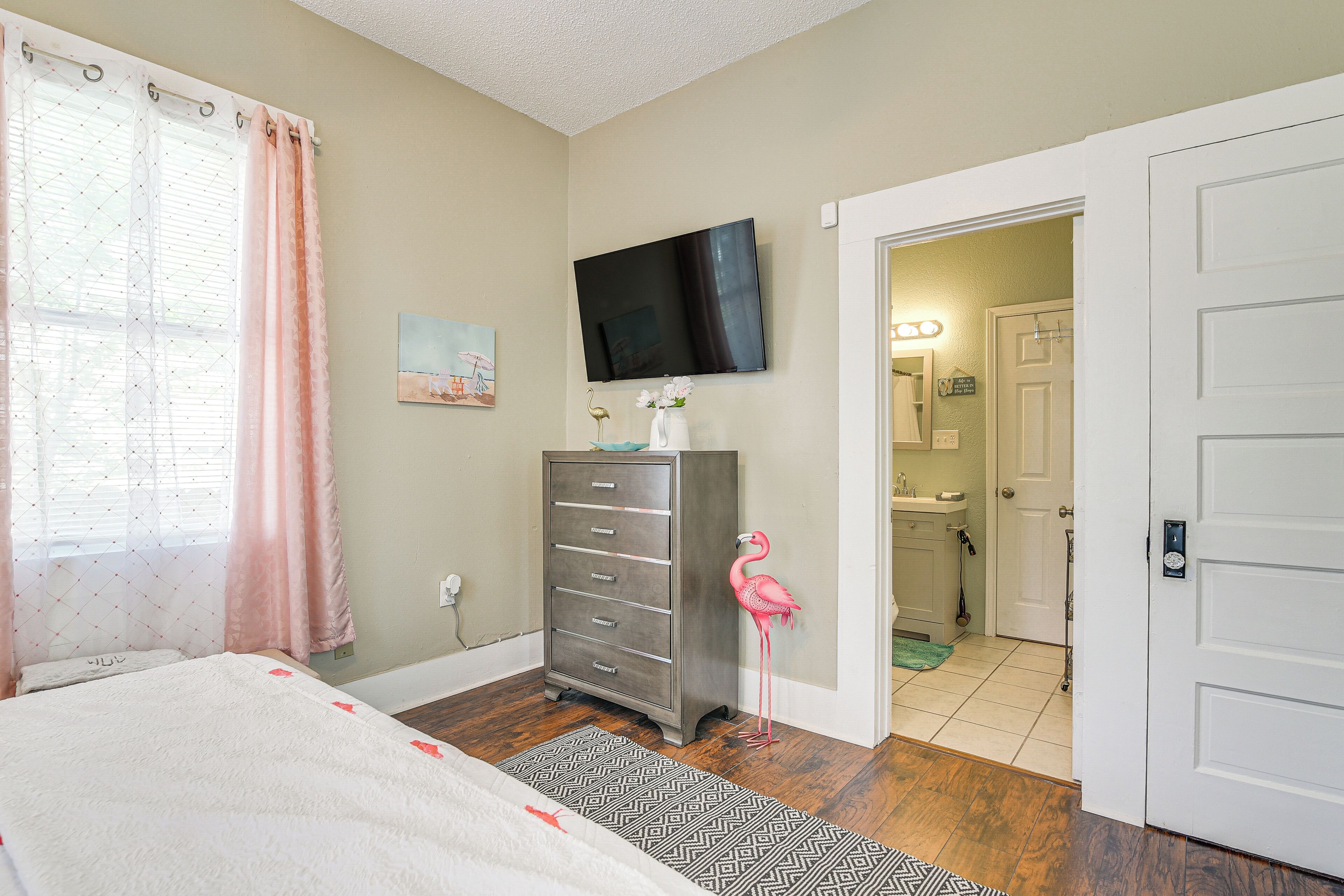 A bedroom with a bed, dresser, TV, and a pink flamingo decoration.