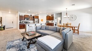 A spacious living area with a large gray sectional sofa, a wooden coffee table, and a dining table with chairs. A kitchen with wooden cabinets and a refrigerator is visible in the background. - Year-round Yuma Escape Near Dtwn: Pets Welcome! (Yuma)