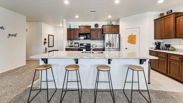 A modern kitchen with a large island, bar stools, wooden cabinets, stainless steel appliances, and a backsplash with a decorative tile pattern. - Year-round Yuma Escape Near Dtwn: Pets Welcome! (Yuma)
