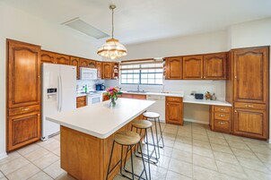 Una cocina amplia con armarios de madera, una isla grande con taburetes, un refrigerador y una lámpara colgante.