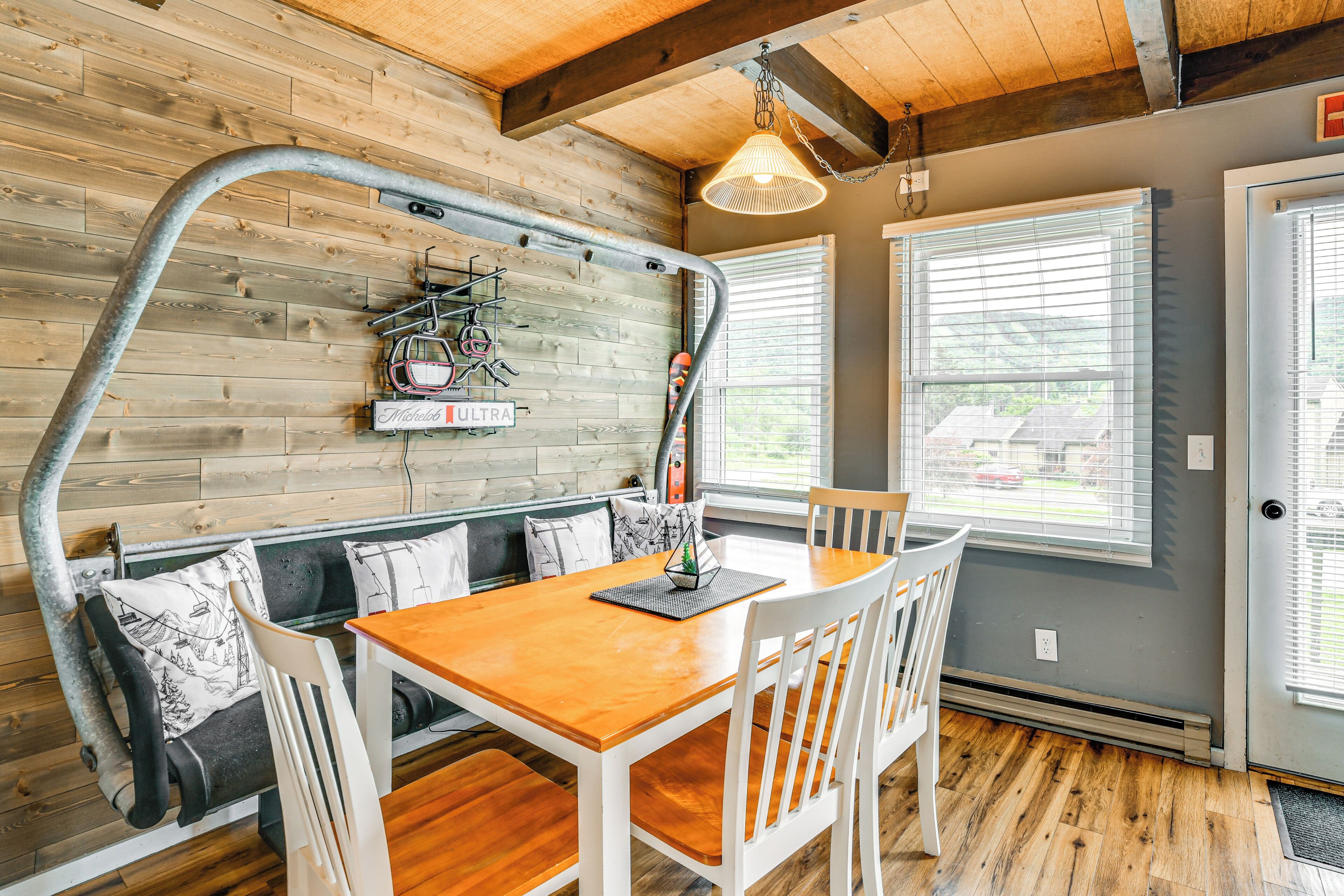 A dining area with a wooden table and white chairs, a bench with cushions, and a wall-mounted bike rack.