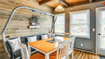 A dining area with a wooden table and white chairs, a bench with cushions, and a wall-mounted bike rack.