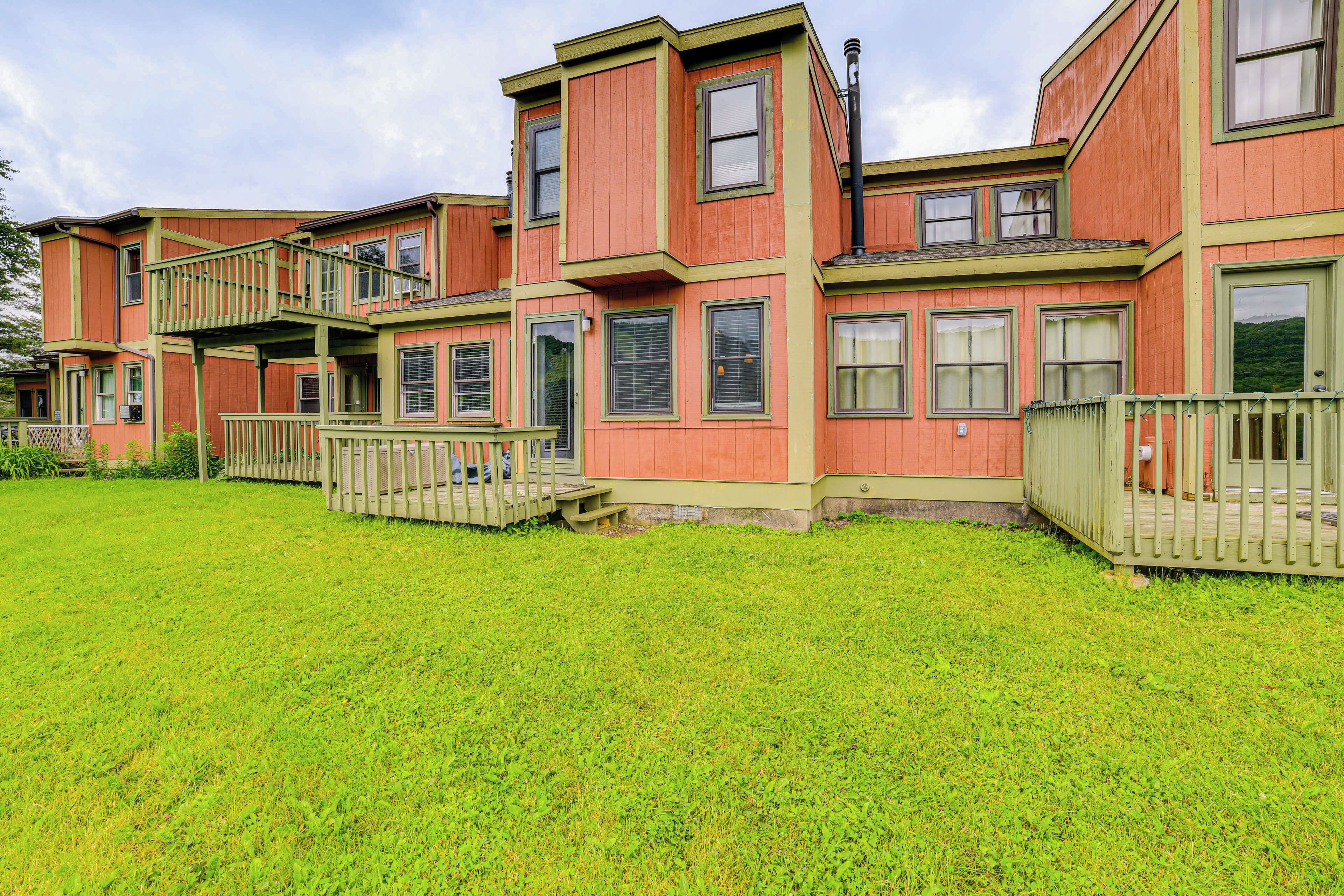 A multi-story residential building with a green and red exterior, a front deck, and a well-maintained lawn.