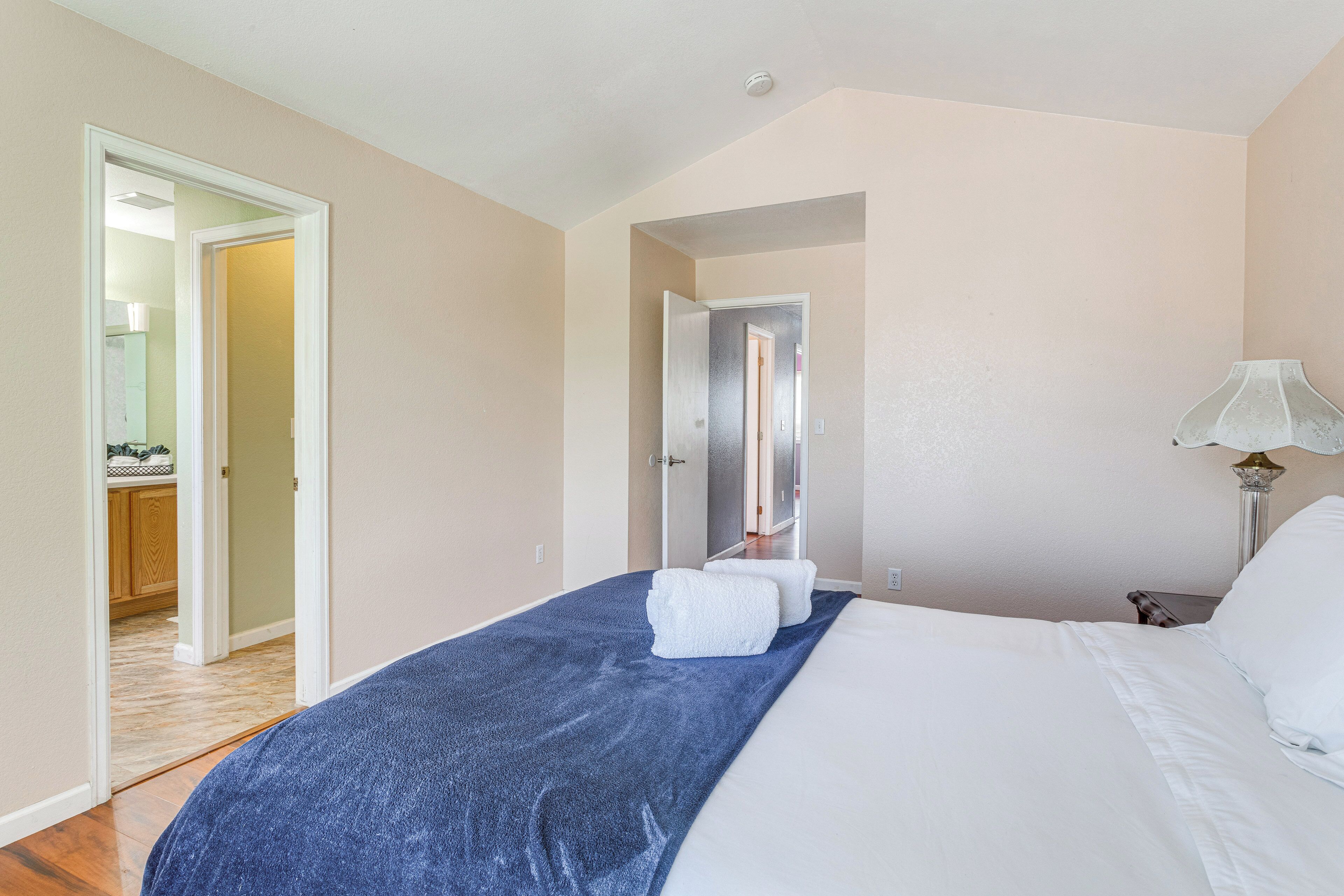 Una habitación de hotel con una cama, una manta azul, almohadas blancas, una mesita de noche con una lámpara y una puerta que da a un baño.