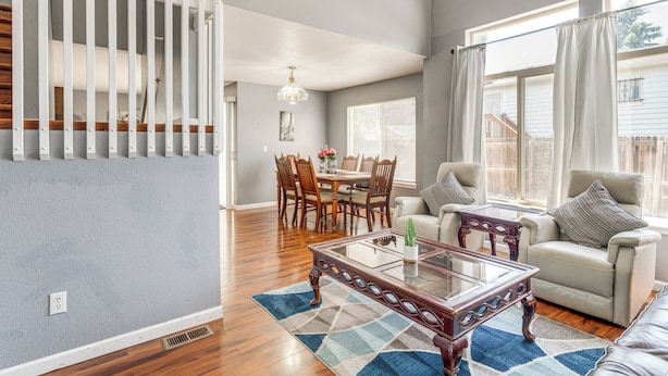 A spacious living room with a high ceiling, a dining area with wooden chairs, and a large window with curtains. - 15 Mi to Downtown Denver: Home w/ Yard + Patio (Aurora)
