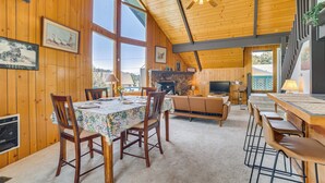 A spacious room with wooden walls and a high ceiling, featuring a dining area with a table and chairs, a sofa, and a fireplace. - Frazier Park Cabin w/ Ping-pong Table, Near Trails (Frazier Park)