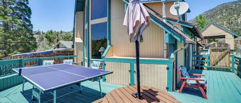 Una terraza de madera con mesa de ping pong, mesa de picnic y dos sillas rojas.