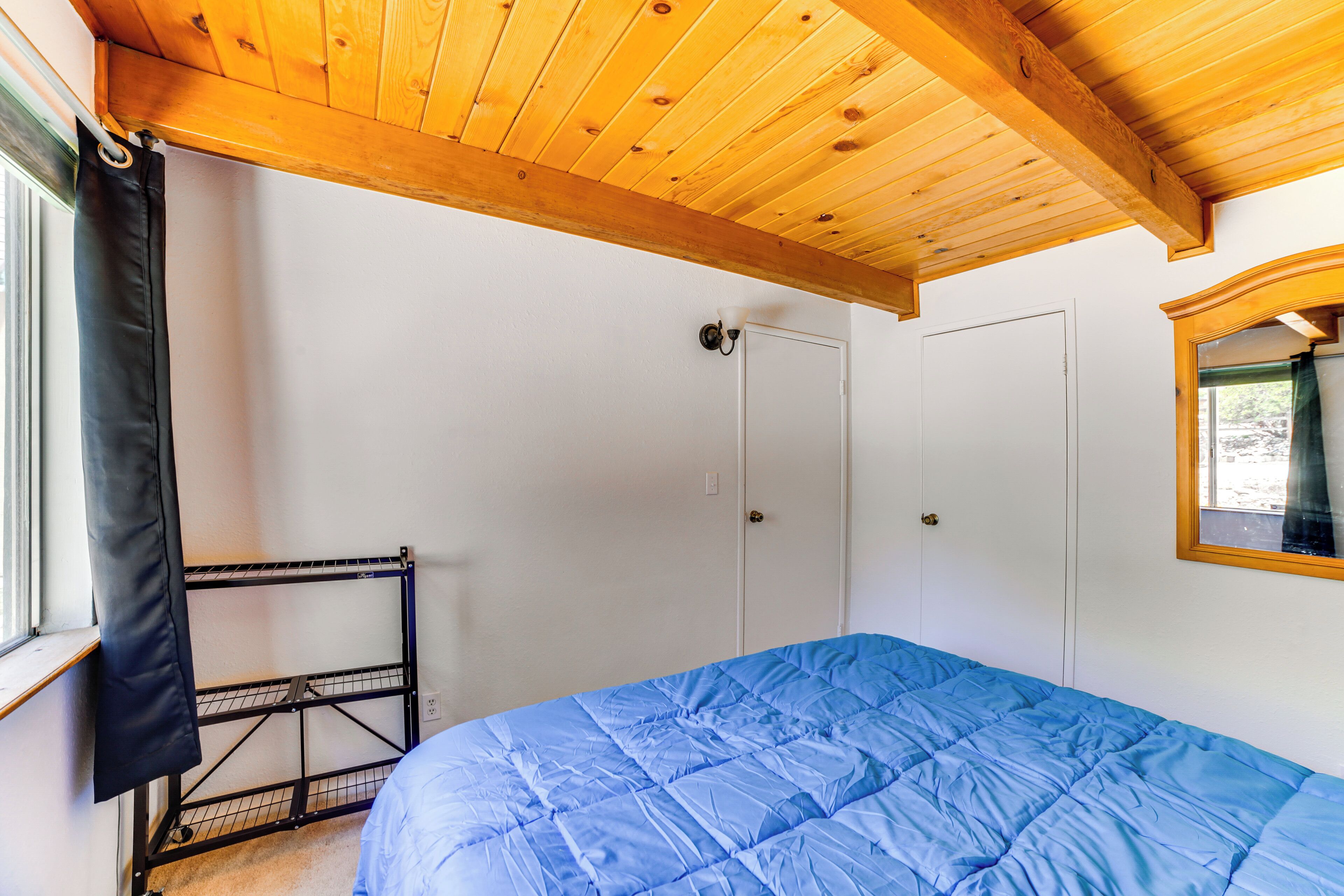 Un dormitorio con techo de madera, colcha azul, estante metálico y puerta blanca.