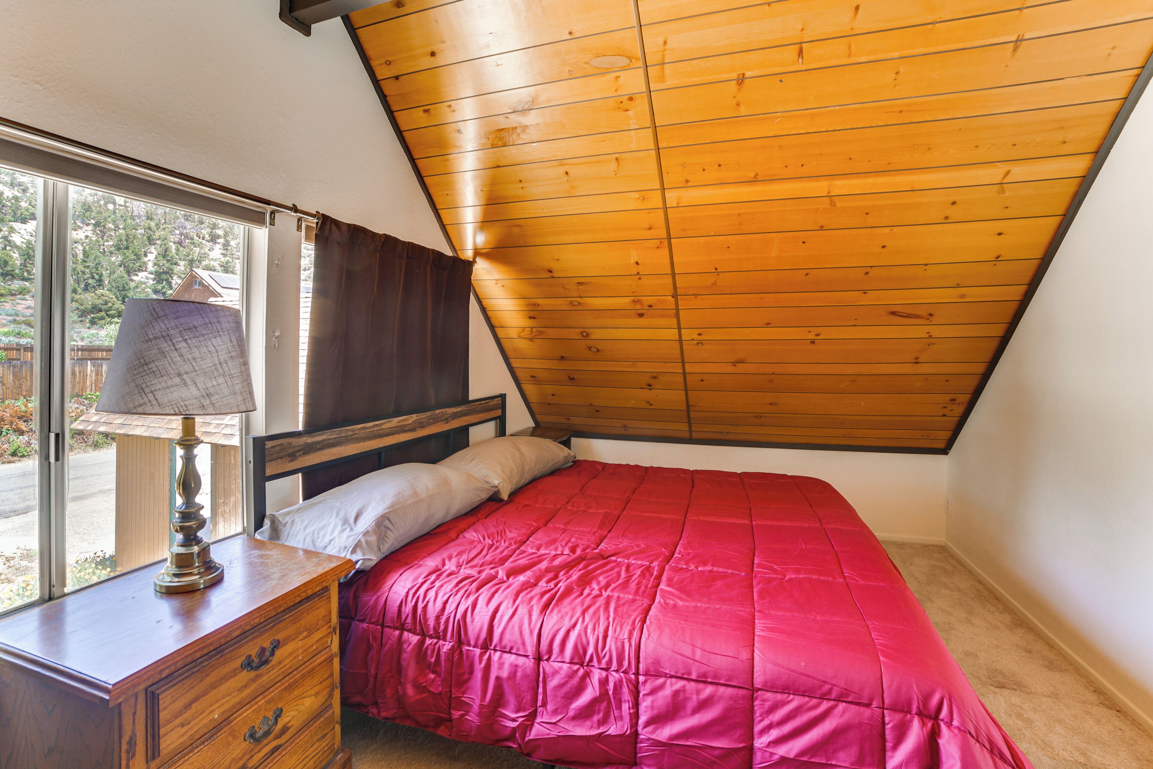 Une chambre avec un plafond en pente, une commode en bois, un lit recouvert d’une couverture rouge et une fenêtre donnant sur l’extérieur.